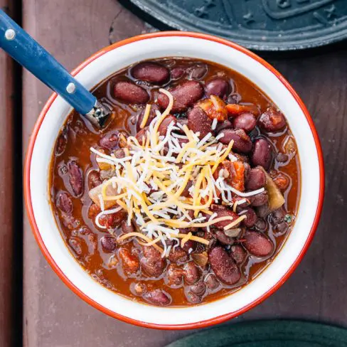 Chili in a white and red bowl topped with shredded cheese.