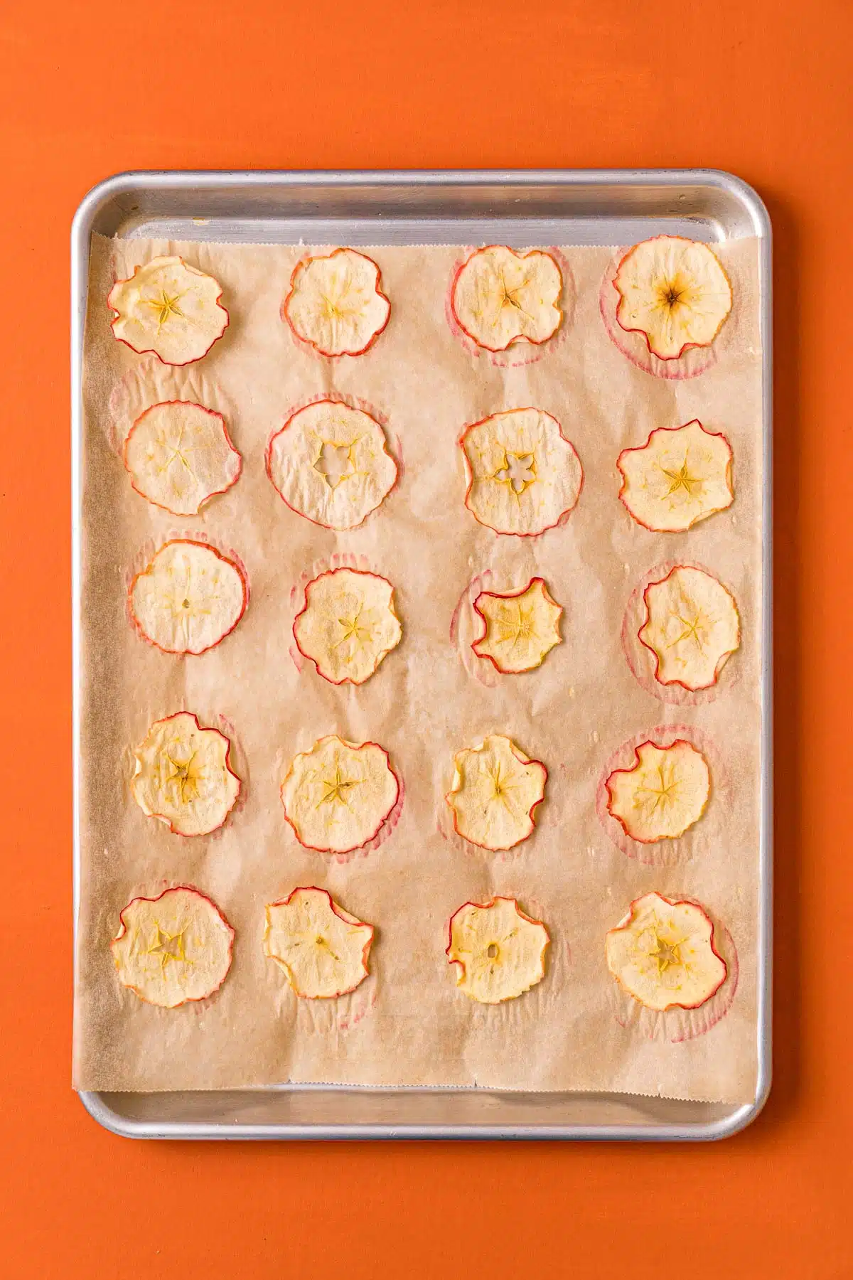 Dried apple chips on a parchment paper lined baking sheet.