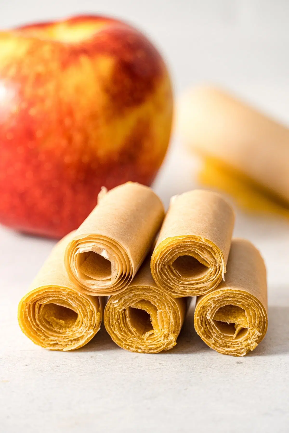 Five fruit rolls stacked in front of an apple