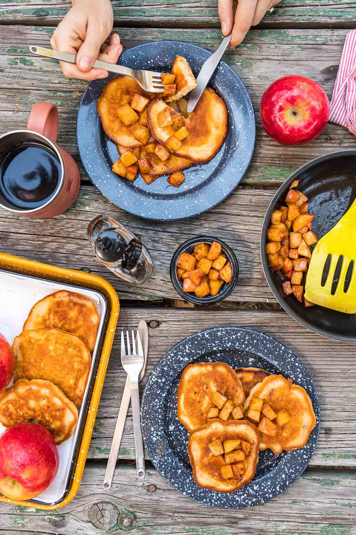 A table scene with two plates of pancakes, coffee cups, and a serving dish with more pancakes in it.