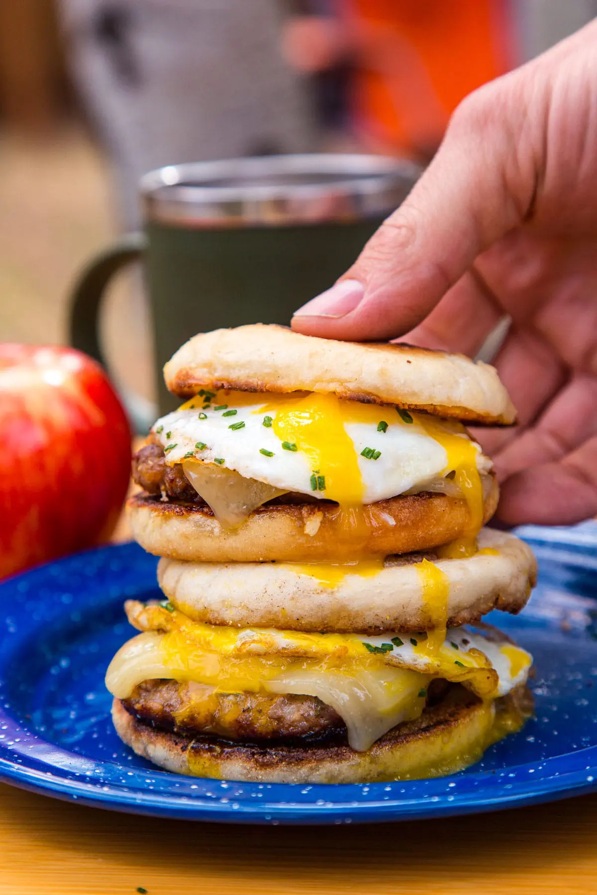 Two stacked breakfast sandwiches on a blue plate. A hand is picking one up.