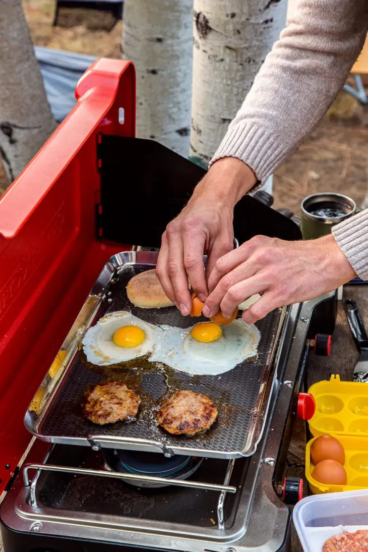 Michael is cracking an egg onto a griddle on a camp stove.