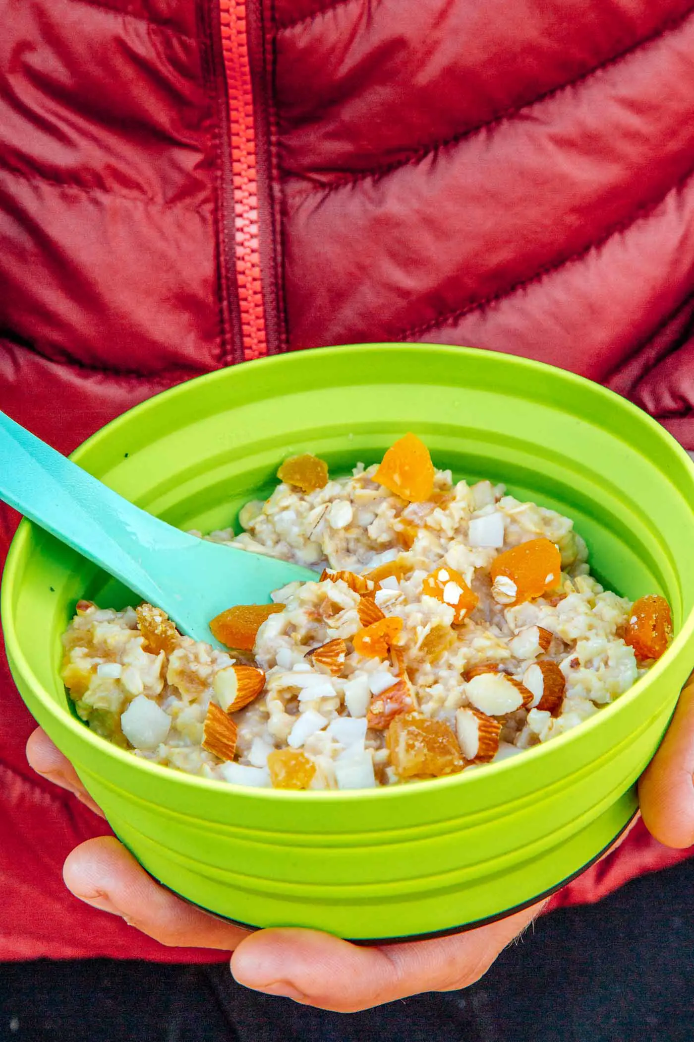 Close up of a man holding a green backpacking bowl full of apricot ginger oatmeal