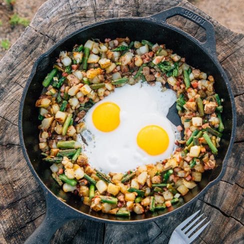 Potatoes, asparagus, and two eggs in a skillet on a stump
