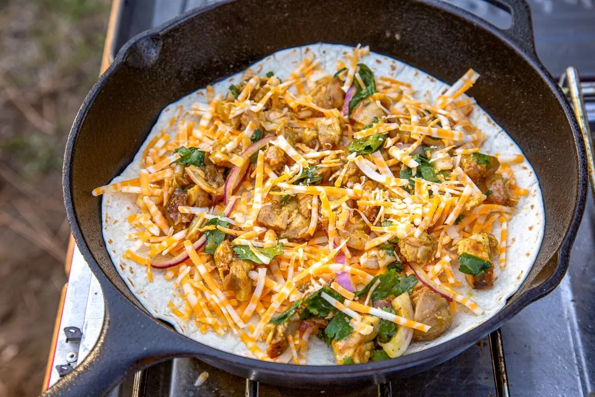 A tortilla topped with BBQ chicken and cheese, in a cast iron skillet.