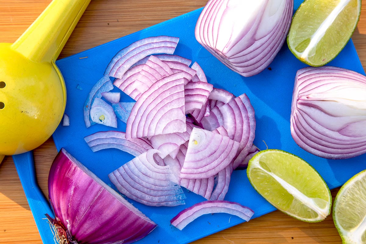 Sliced red onions on a blue cutting board with slices of lime to the side.