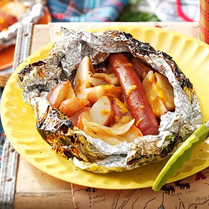 Potatoes and a hot dog in foil served on a yellow plate.