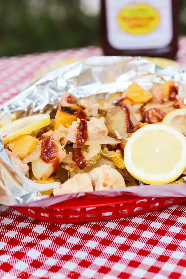 Chicken and pineapple pieces in foil on a red and white checkered table cloth.