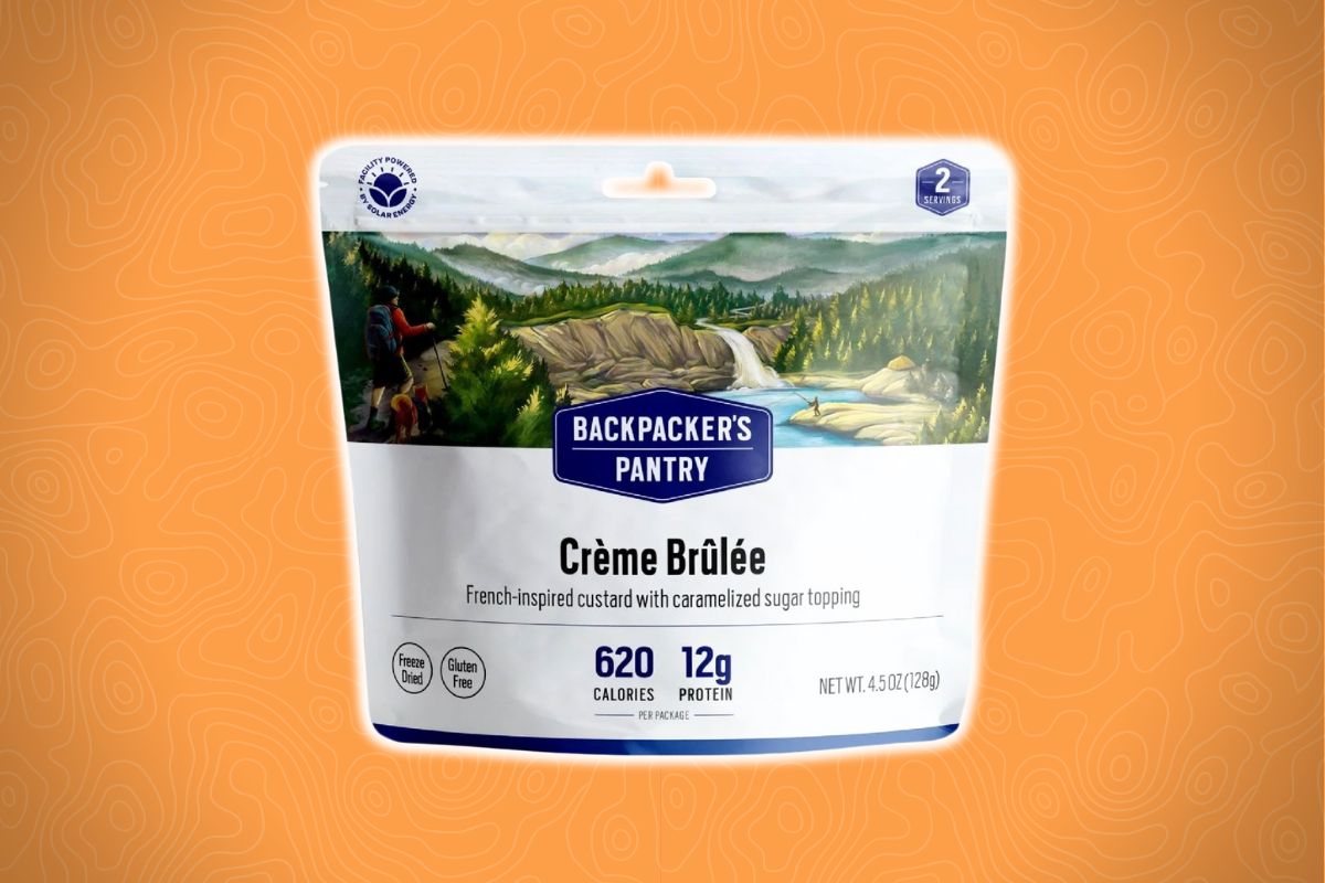 A Backpacker’s Pantry Crème Brûlée dessert package with a mountain illustration sits on an orange background.