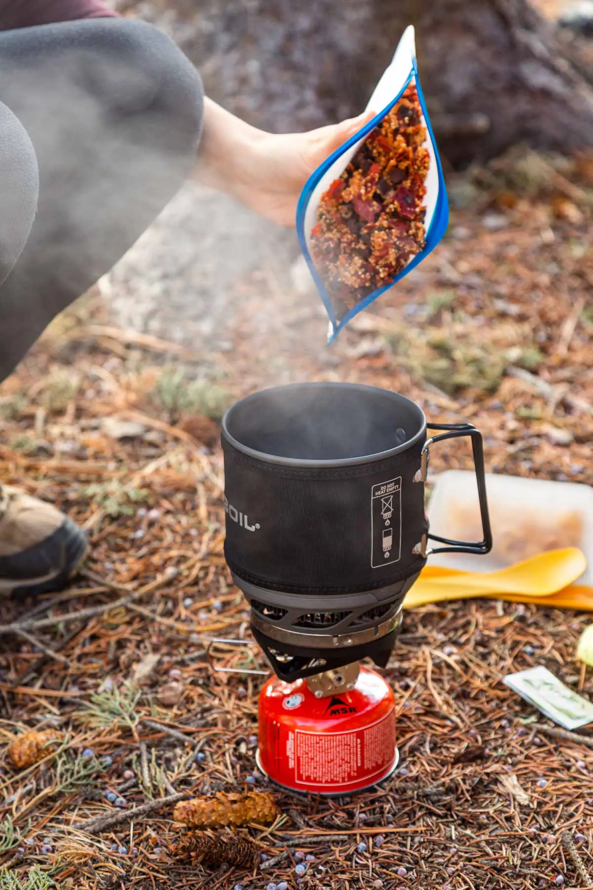 Megan pouring a backpacking meal from bag into a Jetboil stove