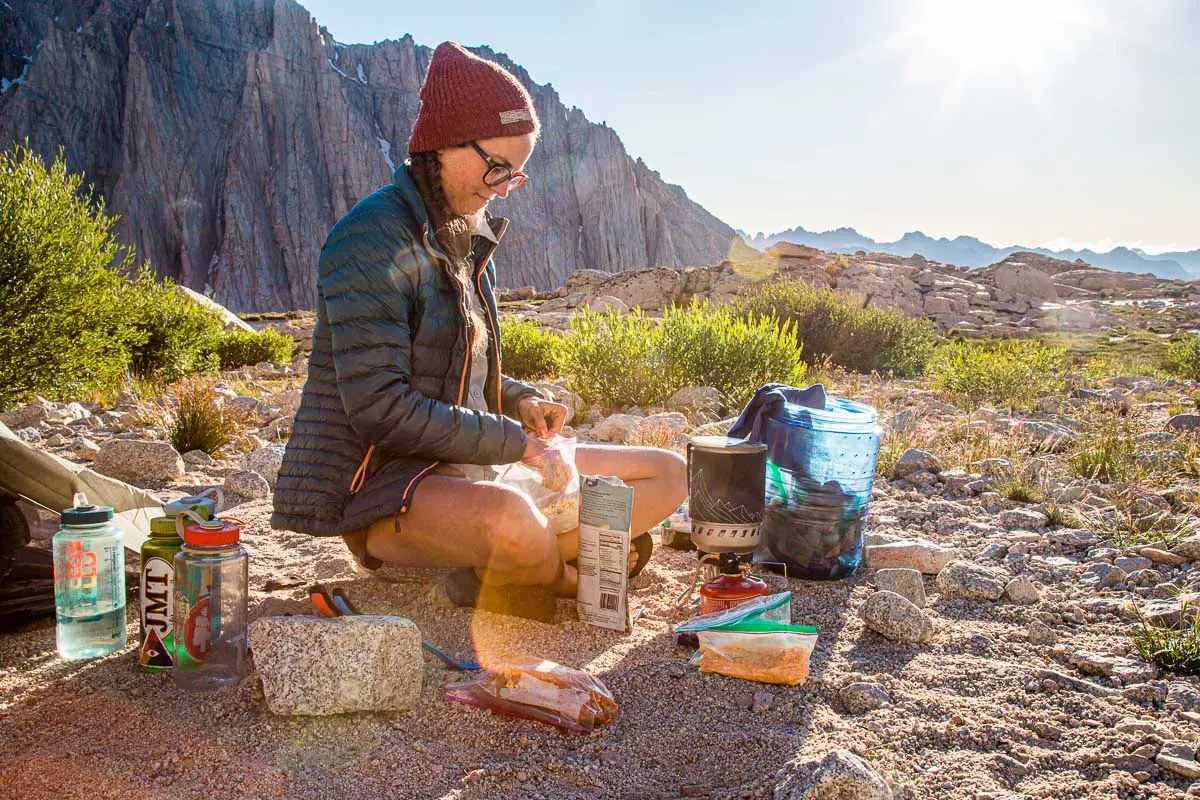 Megan sitting with her backpacking cooking gear at a campsite with mountains in the background