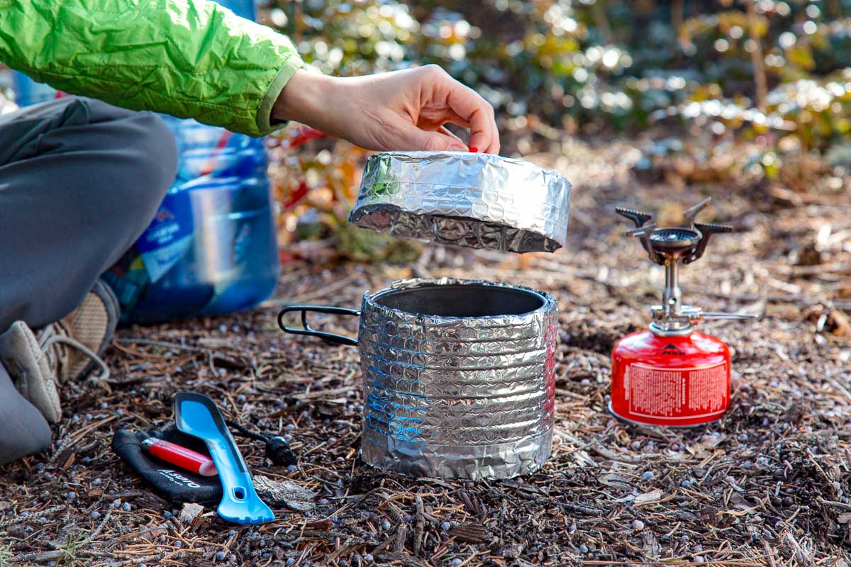 Megan placing the lid on a backpacking pot inside a pot cozy