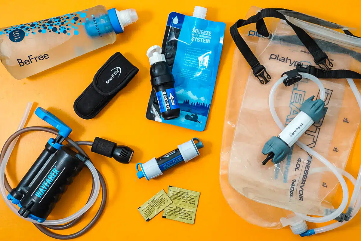 An overhead view of a variety of backpacking water filter options on an orange background.