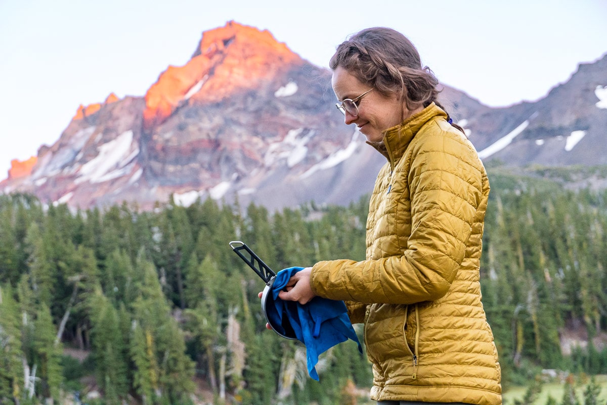 Megan drying a backpacking pot with a mountain in the distance