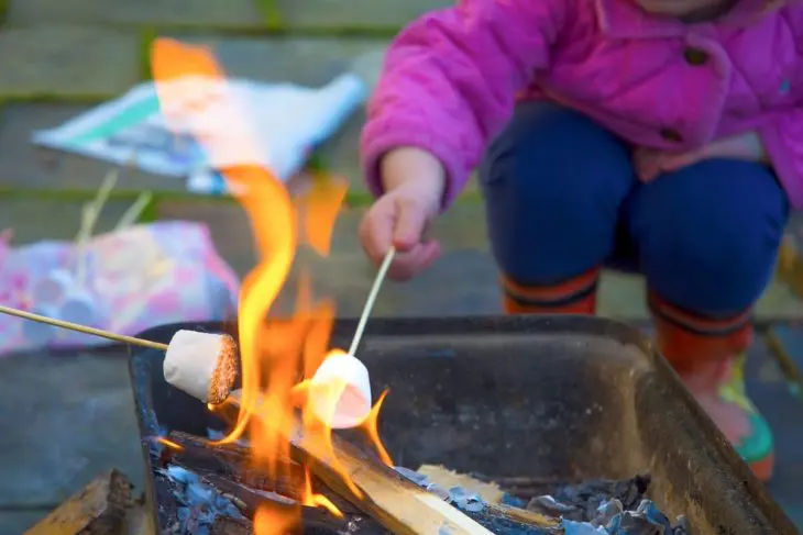 A child roasting a marshmallow over a firepit.