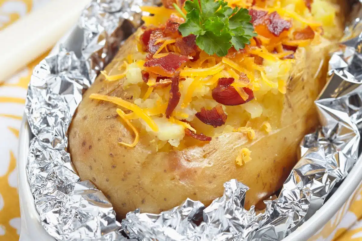 A baked potato with bacon bits and cheese in a foil packet.