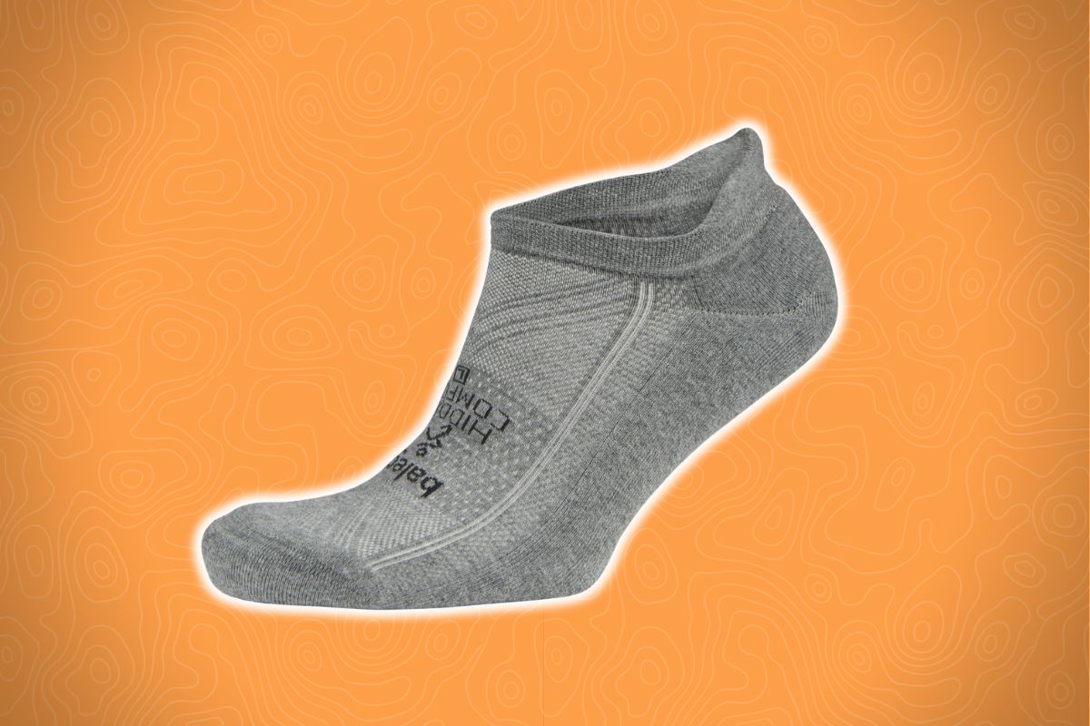 A single gray ankle sock with visible stitching and side text lies on an orange background with a wavy line pattern.
