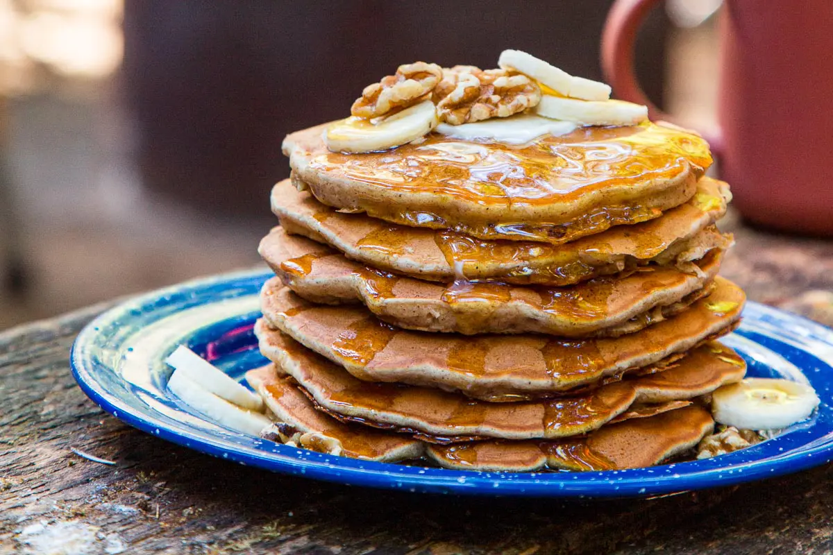 A stack of pancakes on a blue plate, topped with slices of bananas and walnuts.