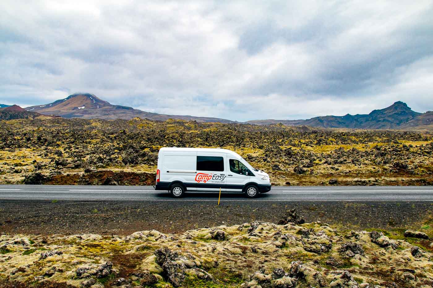 A white camper van on a road between mossy lava fields