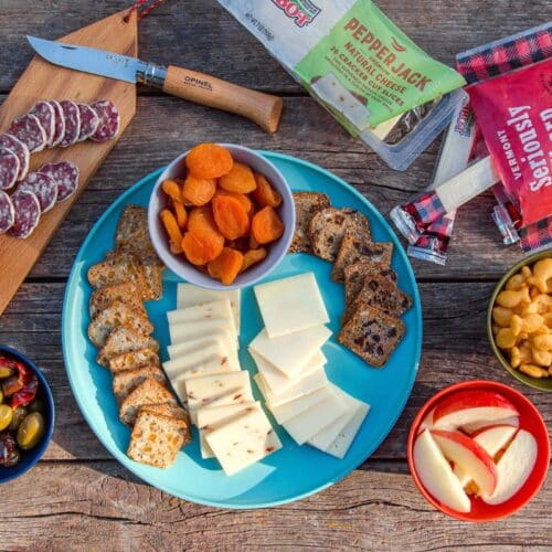Cheese, fruit, salami, nuts, and crackers displayed on a camping table.
