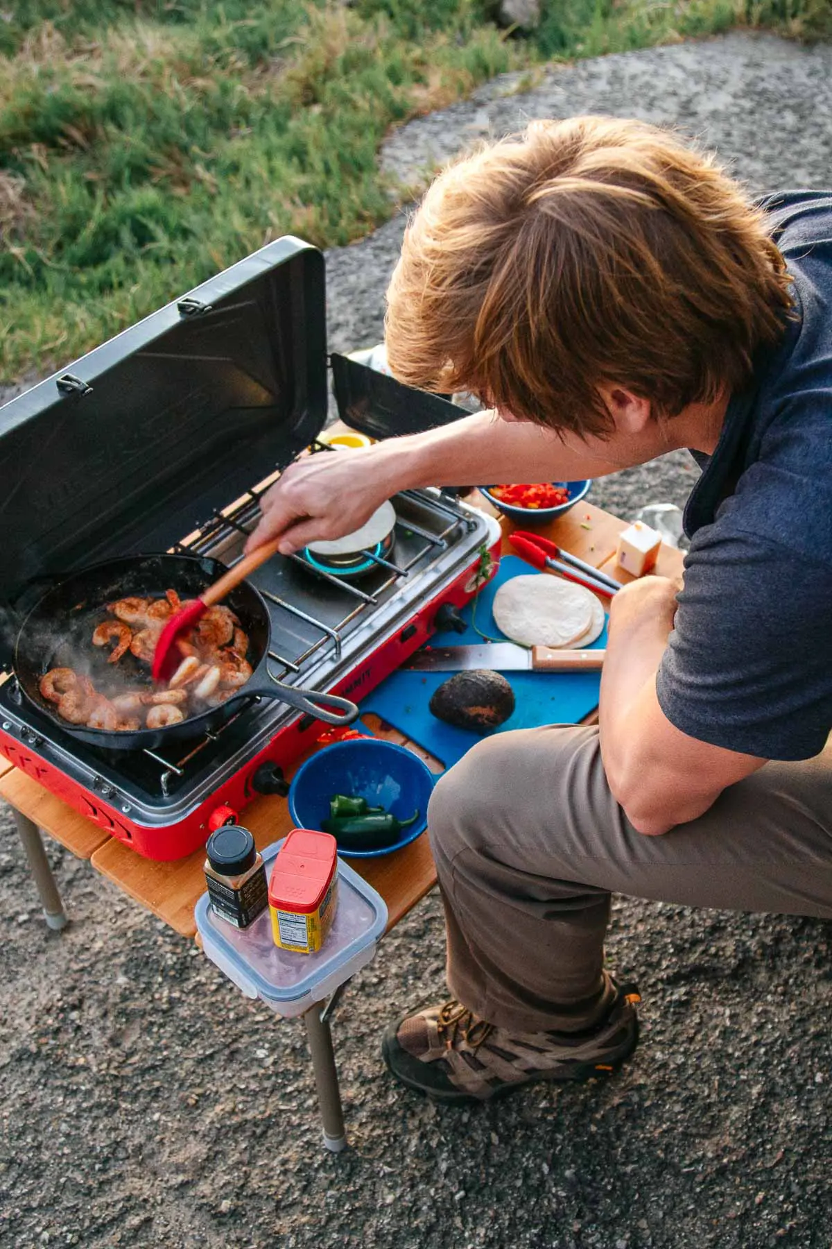 Michael cooking shrimp in a cast iron skillet on a camp stove.