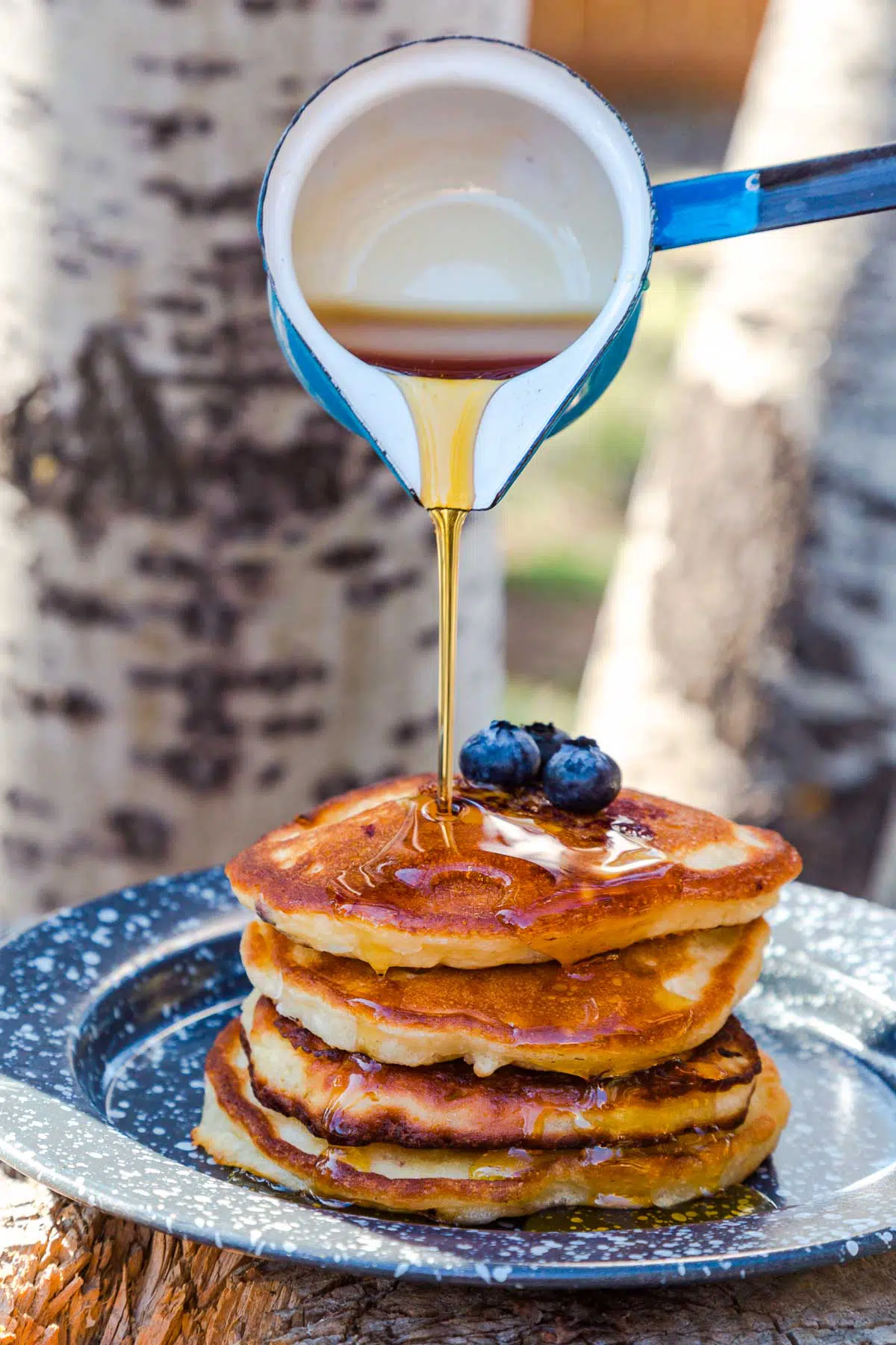 Pouring maple syrup over a stack of blueberry banana pancakes