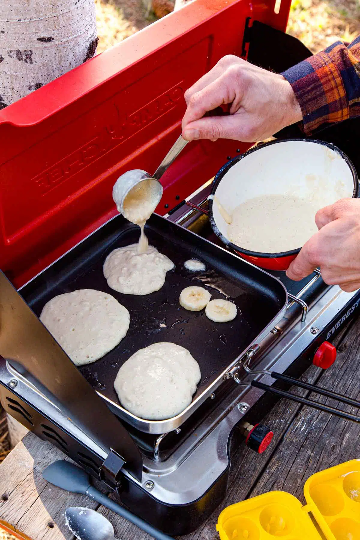 Michael adding pancake batter to a griddle on a camping stove