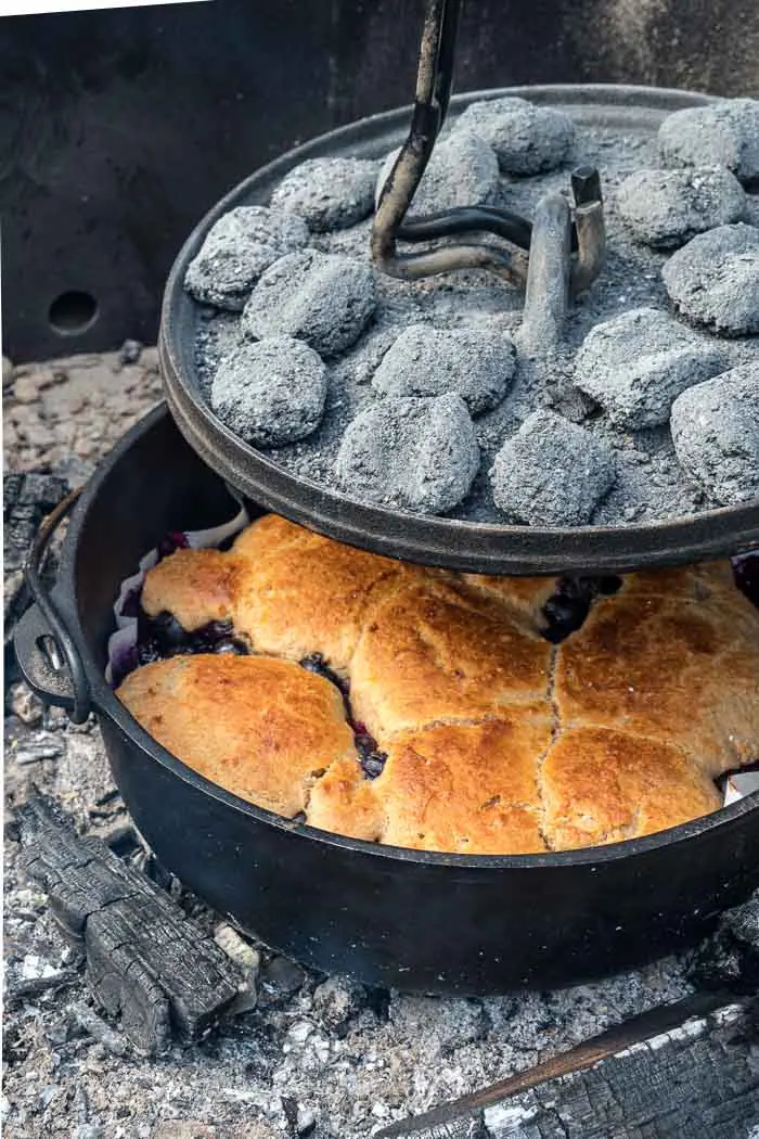 Lifting a dutch oven lid to reveal cobbler
