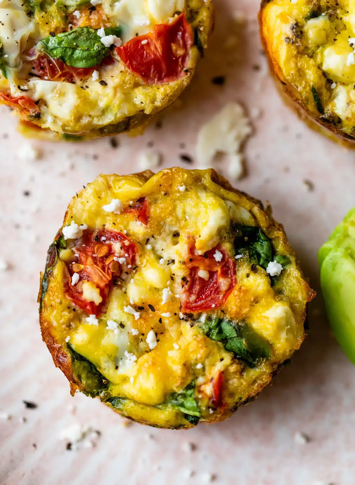 A close-up reveals vibrant, colorful egg muffins containing spinach, tomatoes, and cheese, perfectly baked.