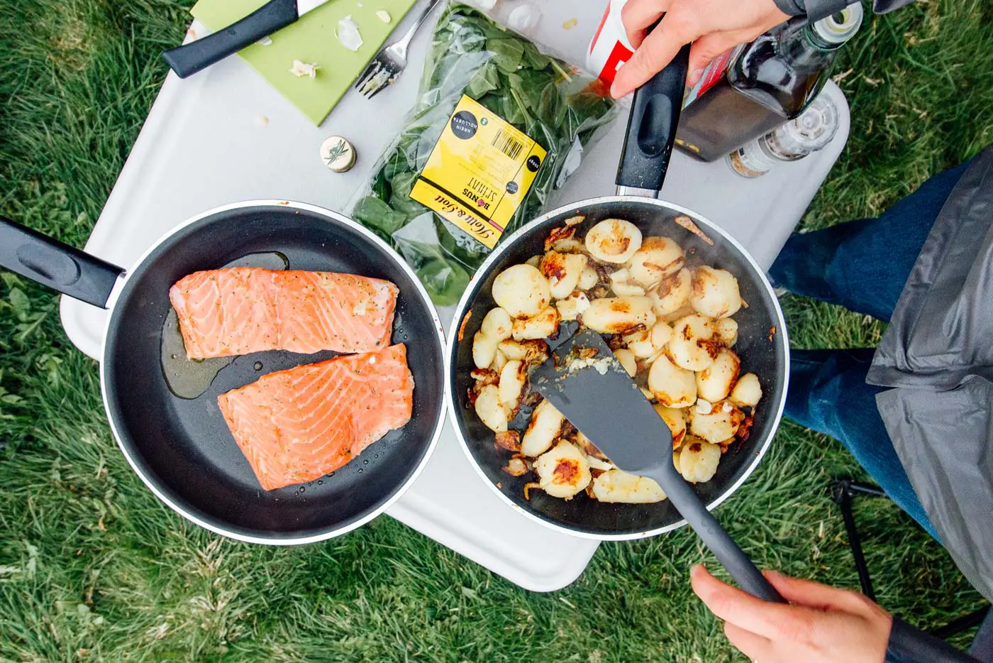 Overhead view of two skillets containing potatoes and salmon on a camping table