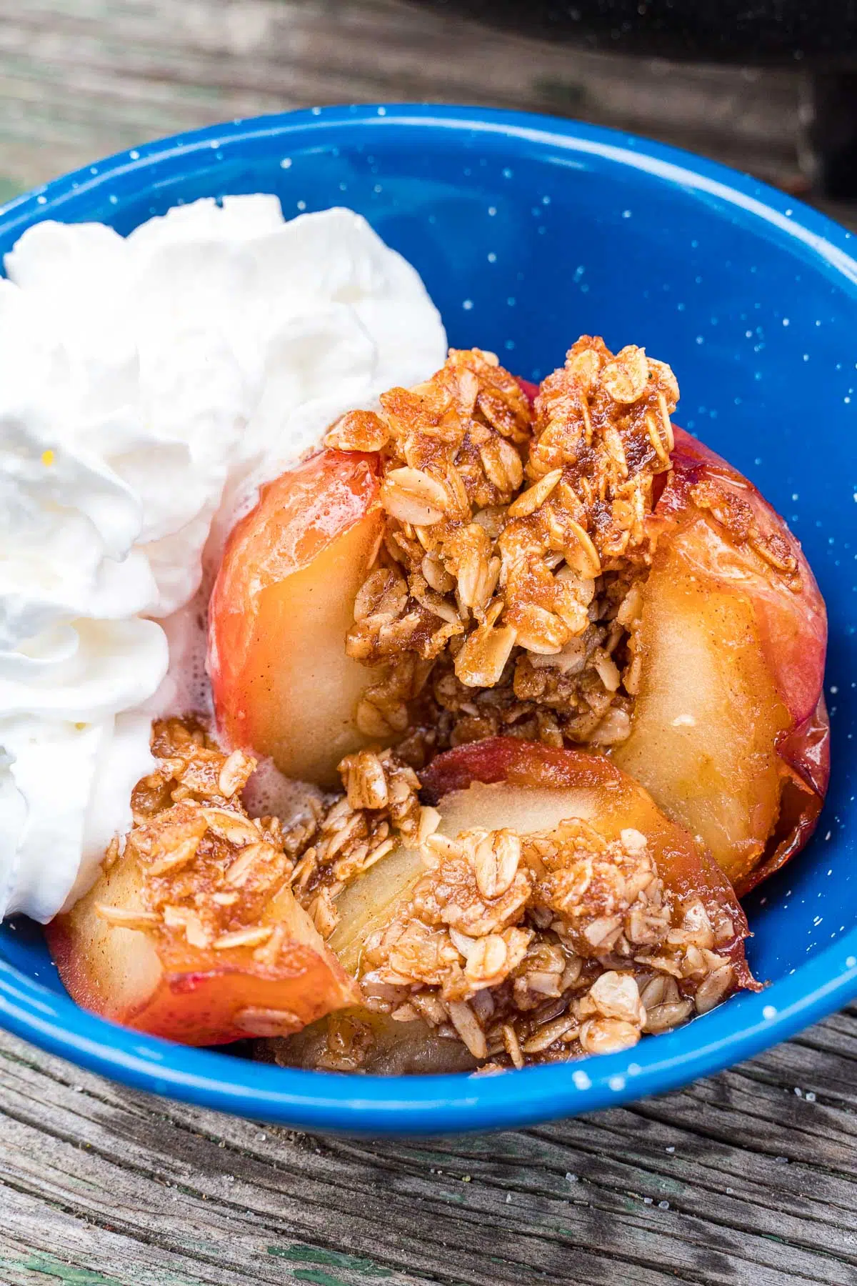 An apple filled with oats in a bowl with whipped cream.