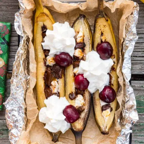 Campfire banana splits topped with whipped cream in a serving dish