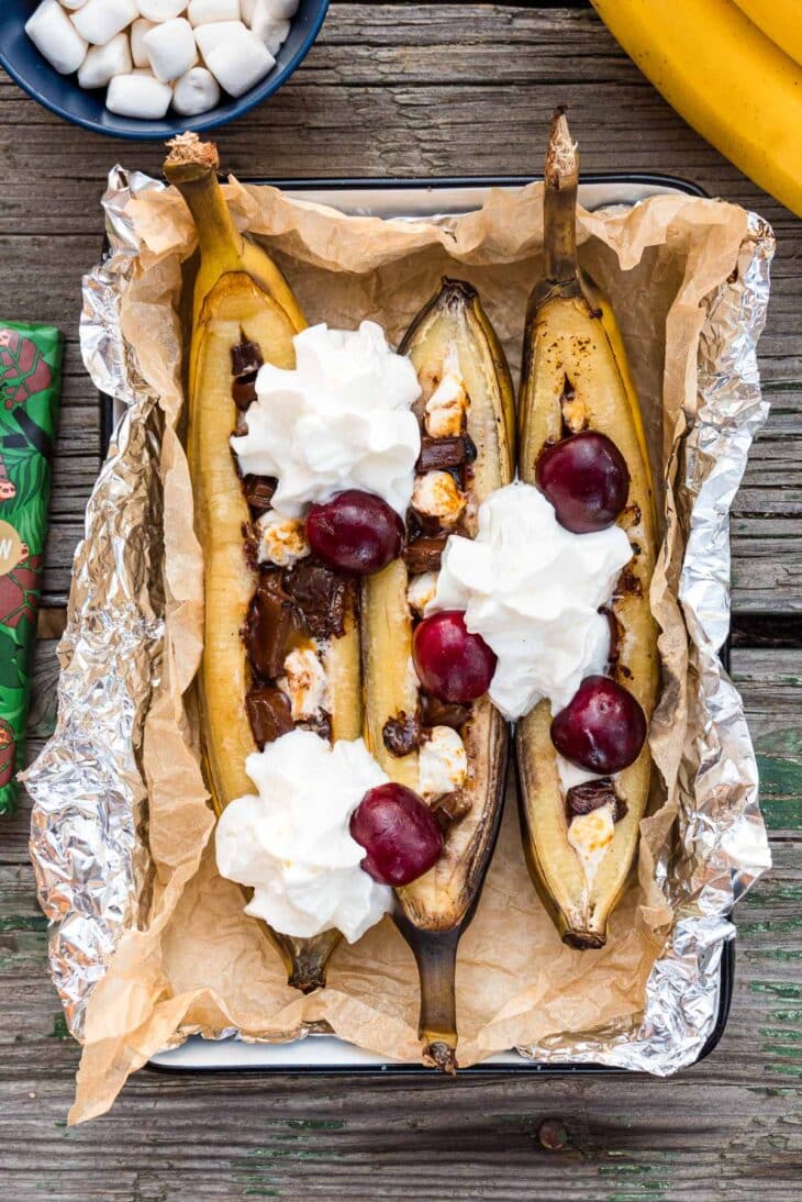 Campfire banana splits topped with whipped cream in a serving dish
