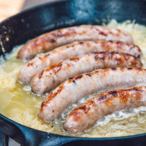 Beer brats simmering in beer and sauerkraut in a cast iron skillet