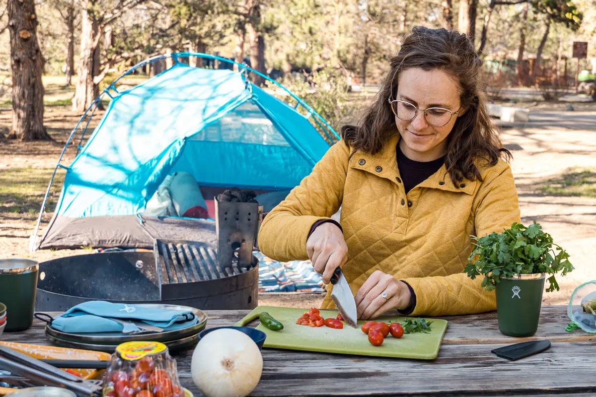Megan chopping ingredients for tacos with a camp scene in the background