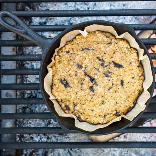 A chocolate chip cookie in a cast iron skillet over a campfire