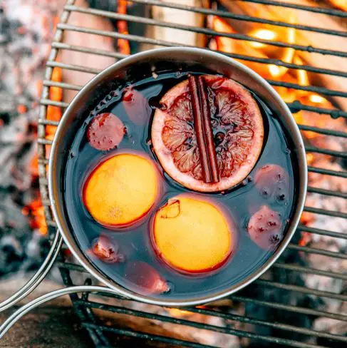 Wine with oranges and a cinnamon stick in a pot over a campfire