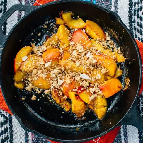 Sliced peaches topped with granola in a skillet