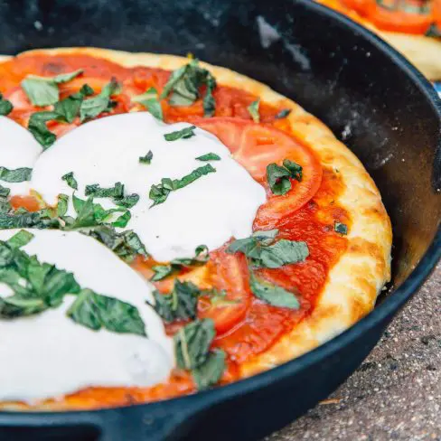Pizza topped with mozzarella cheese slices and basil in a cast iron skillet