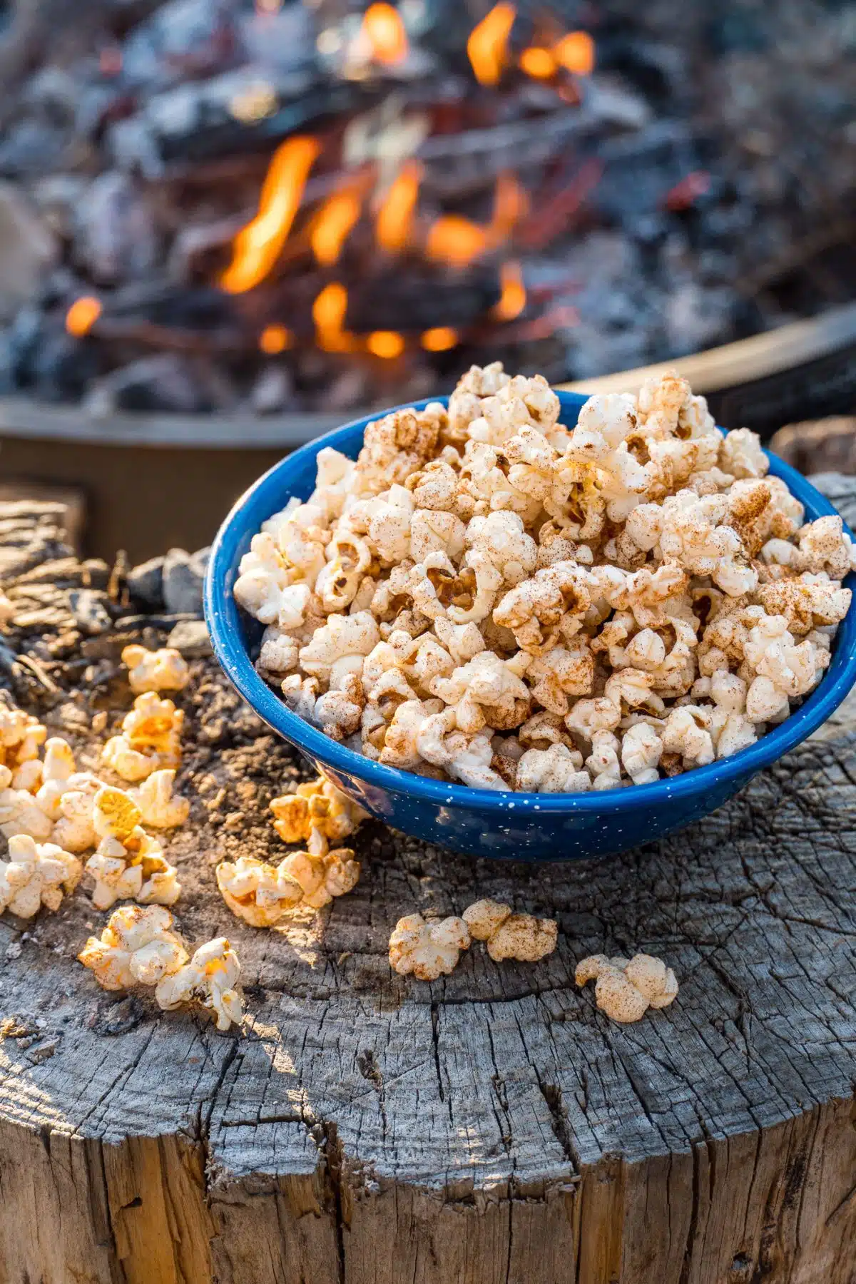 Popcorn in a blue bowl with a campfire in the background.