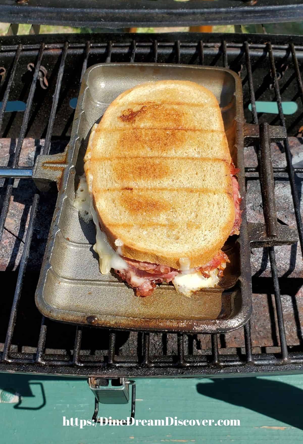 A grilled Reuben sandwich in a pie iron on a grill.
