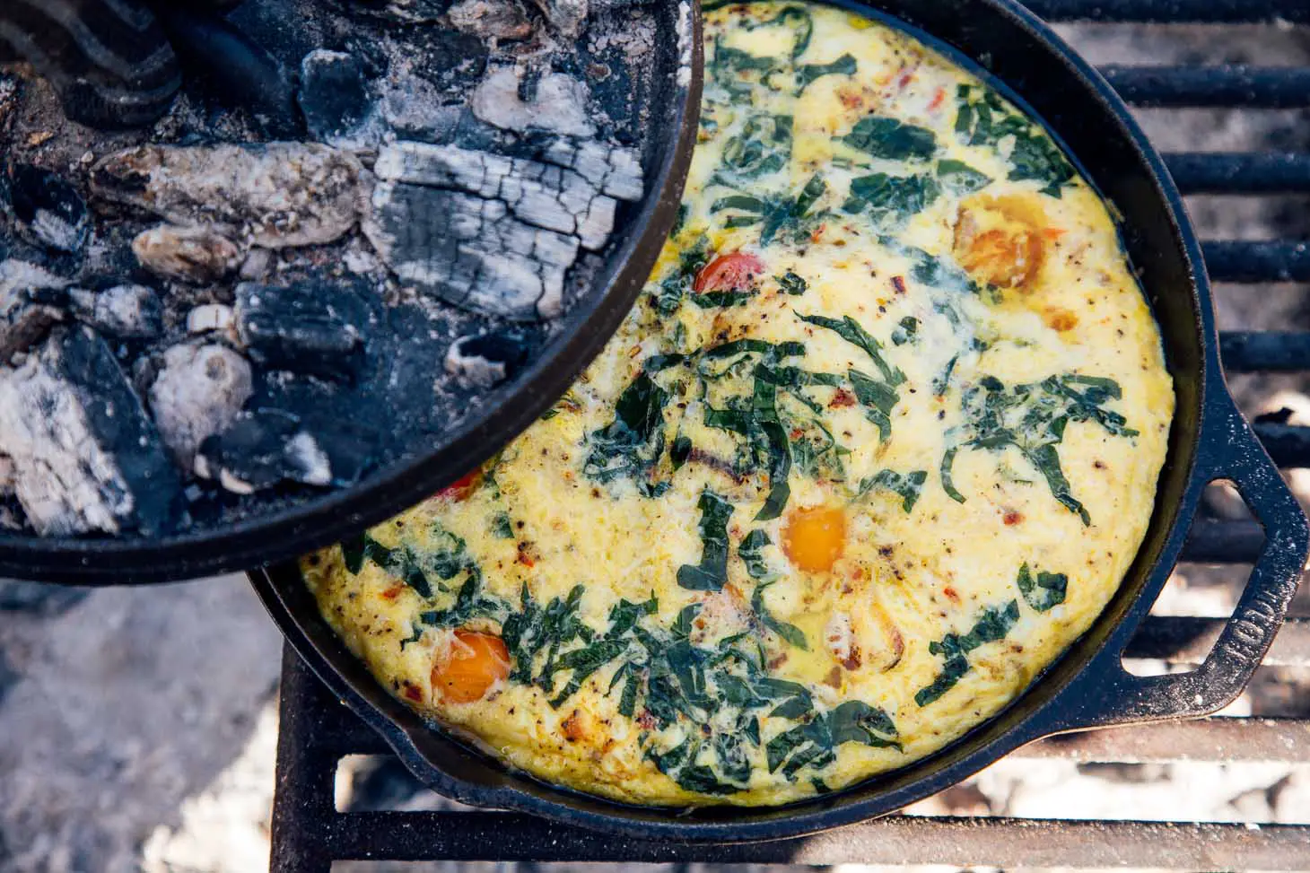 Lid to a cast iron skillet being removed to reveal a vegetable frittata.