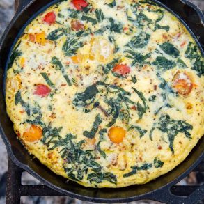 Vegetable frittata in a cast iron skillet over a campfire.