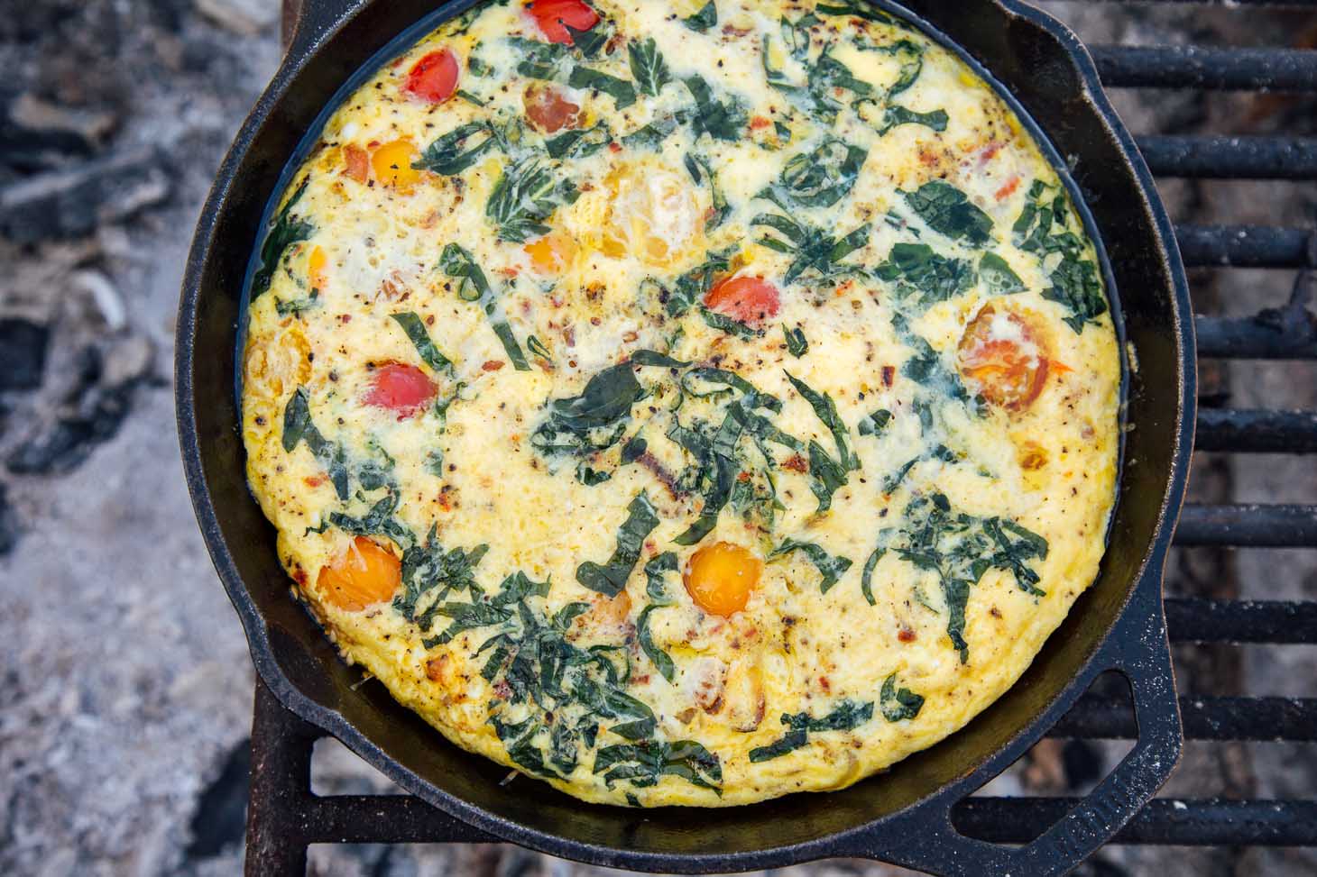 Vegetable frittata in a cast-iron skillet over a campfire.