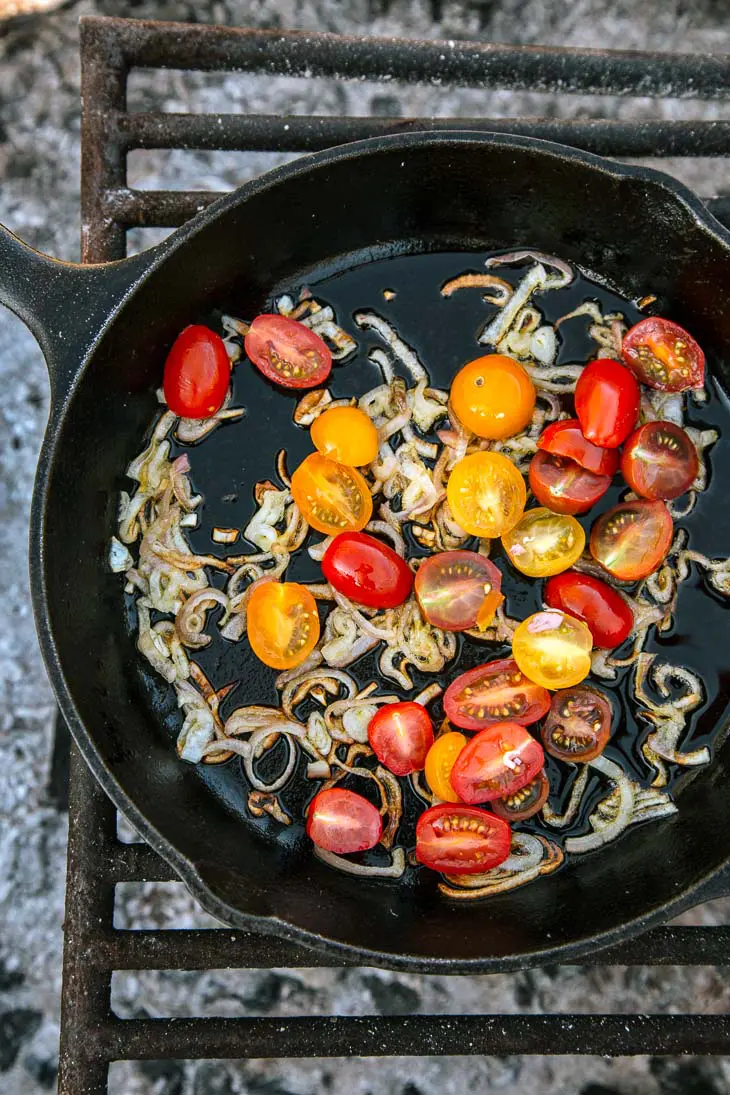 Cherry tomatoes and shallots in a cast iron skillet over a campfire
