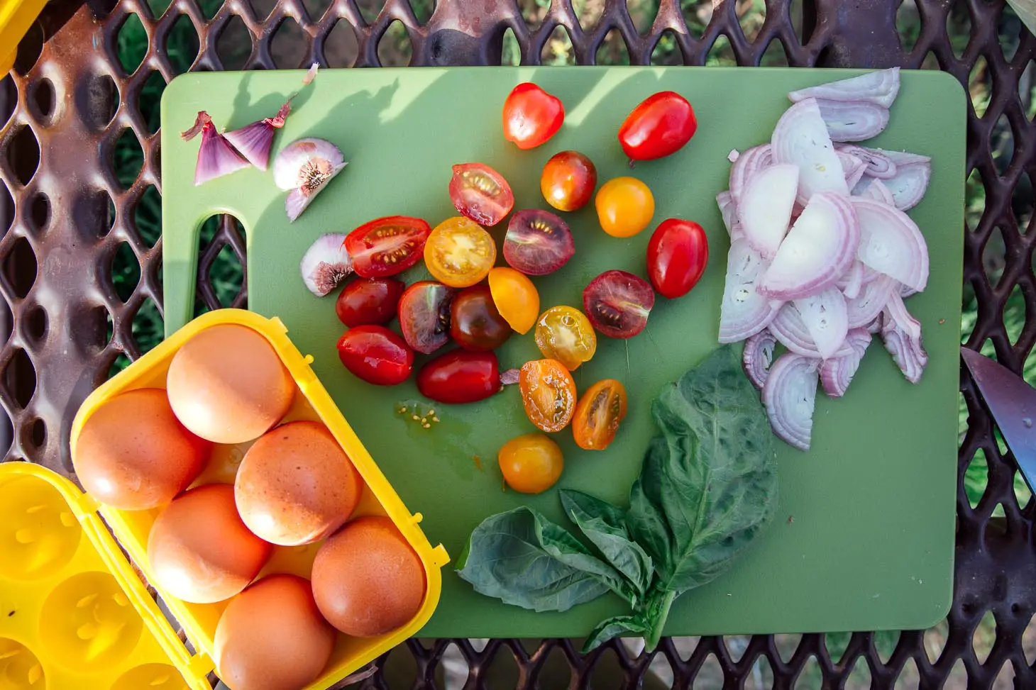 Ingredients for frittata: eggs, tomatoes, shallots, garlic, basil laid out on a cutting board.