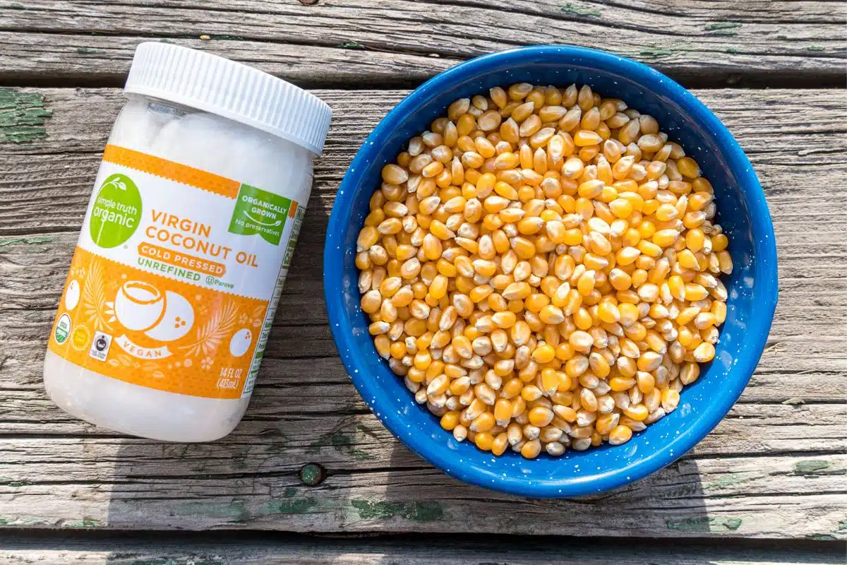 A jar of coconut oil next to a bowl of popcorn kernels.