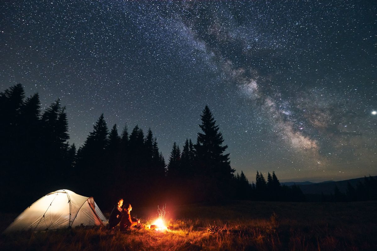 A couple sitting next to a tent and a campfire under a starry sky