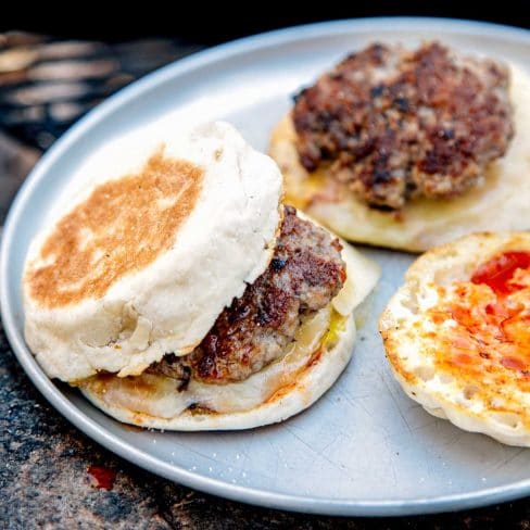 Two sausage patties on english muffins on a silver plate