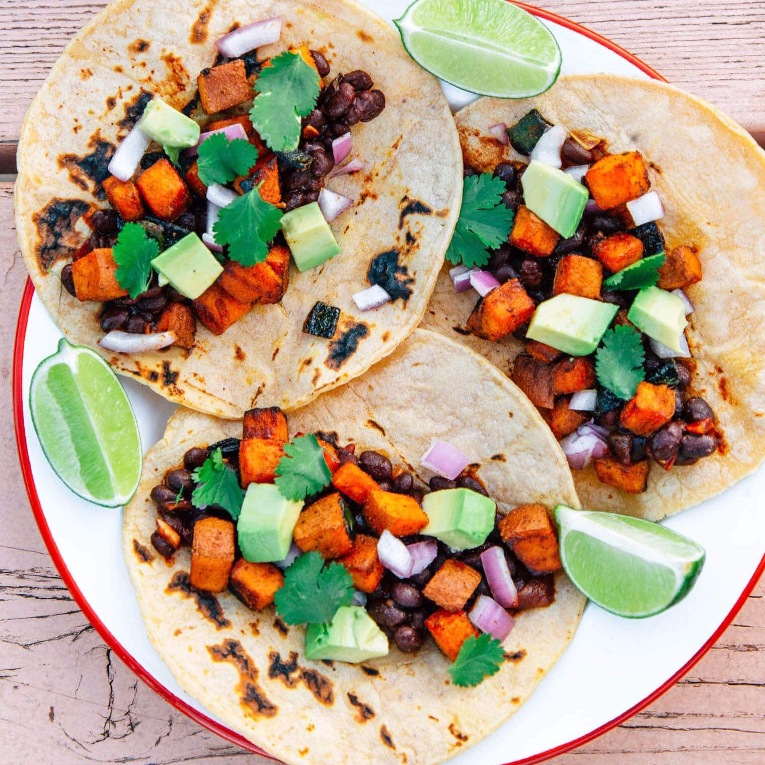 Three tacos on a plate filled with black beans, sweet potato, and avocado